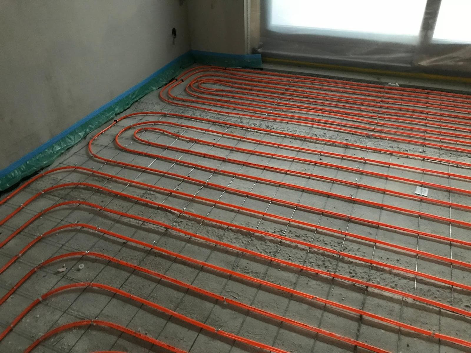 Vloerverwarming met oranje leidingen netjes aangelegd op betonvloer met blauwe randisolatie