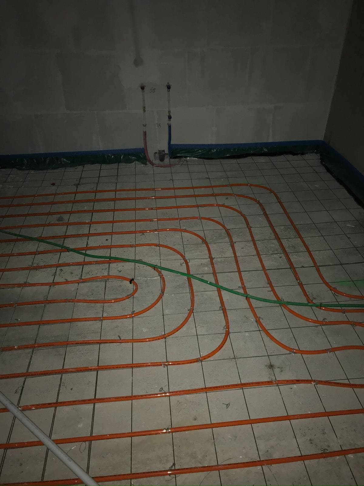 Vloerverwarming met oranje leidingen in spiraalmotief op tegelvloer